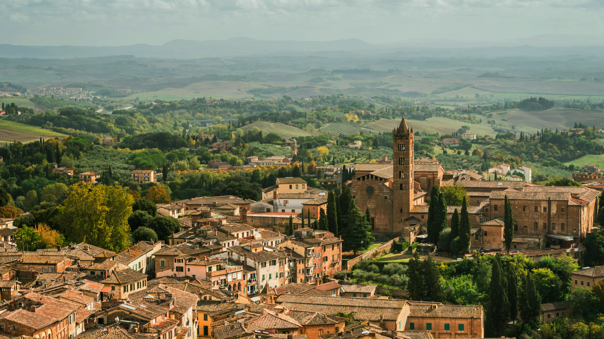 Historic Tuscan town with terracotta rooftops and church tower overlooking rolling countryside in Tuscany, Italy